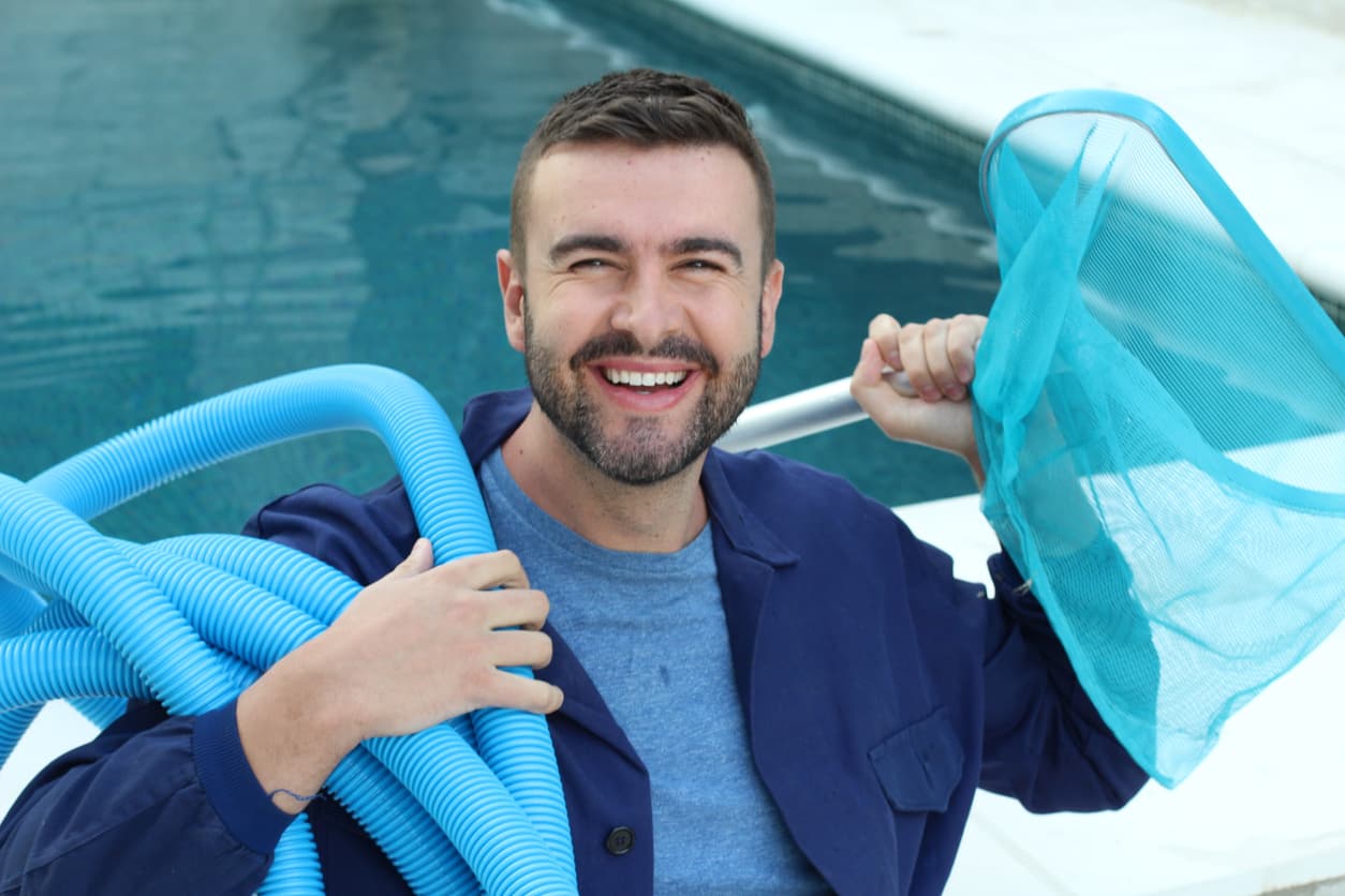 A smiling pool man holding maintenance equipment smiles after becoming an expert in his field