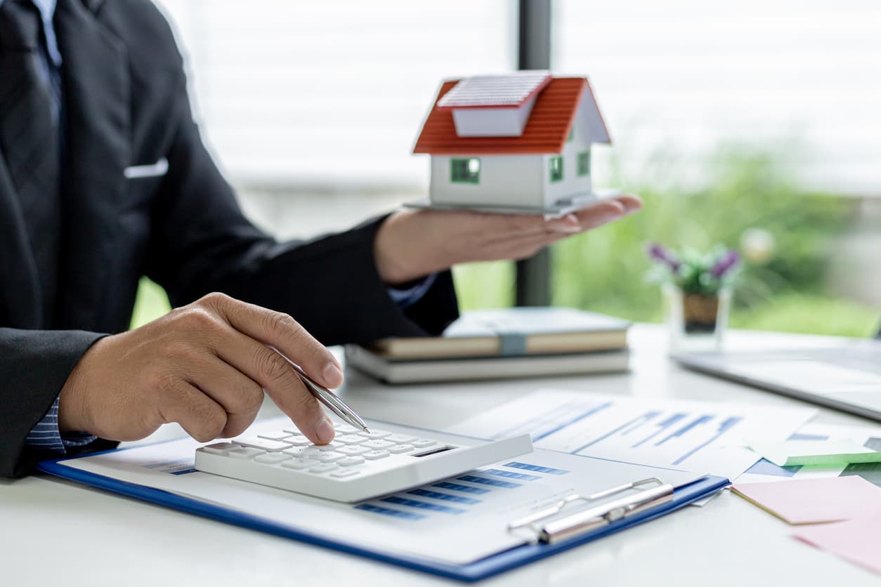 A businessman holds a small model house and makes calculations to avoid property manager mistakes