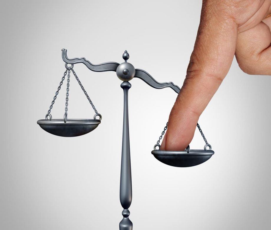 A hand tips a mini scale as a representation of selective enforcement