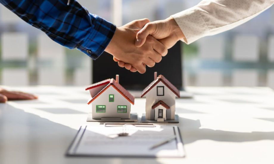Two people shaking hands over some models of housing.