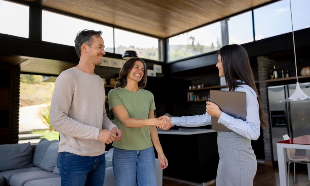A community management professional shaking hands with a couple looking at a home.