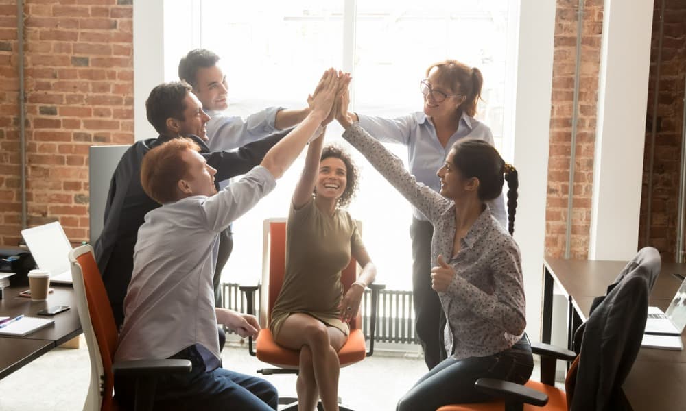 A group of motivated, happy, diverse office people giving each other high fives.